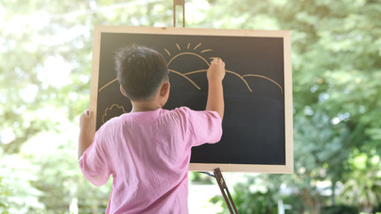 Asian boy people who are creative, drawing the mountain with the sun on black chalk board.  tree...