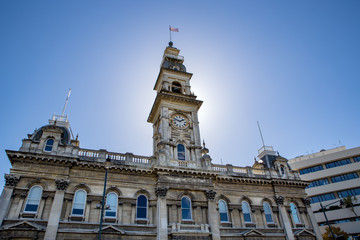 Fototapeta na wymiar The clock tower on an old stone building in the city of Dunedin is lit up in the sunlight