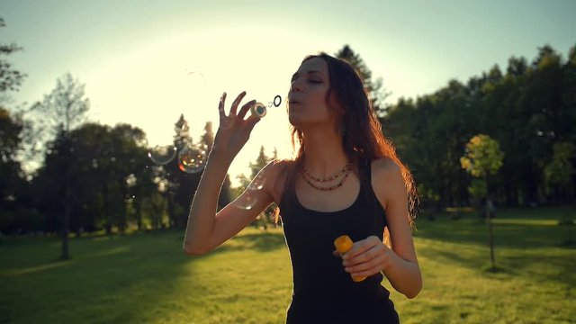 Portrait of beautiful redhair young woman. Blowing bubble in the park. Super slow motion shot in 180 fps. Sunrise or sunset straight orange light.