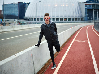 Teenage boy doing stretching exercise while warming upon track before running