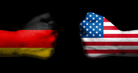 Flags of Germany and United States painted on two clenched fists facing each other on black...