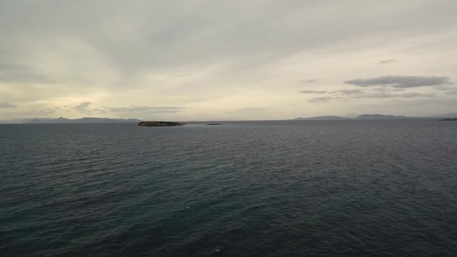 Flying over the sea on a cloudy day. Small island on the horizon.