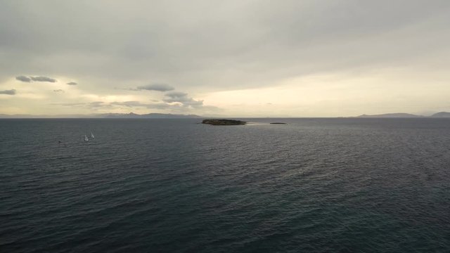 Flying over the sea on a cloudy day. Small island on the horizon.