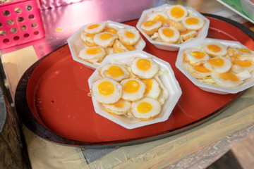 Fried quail eggs in geometric foam container at market.