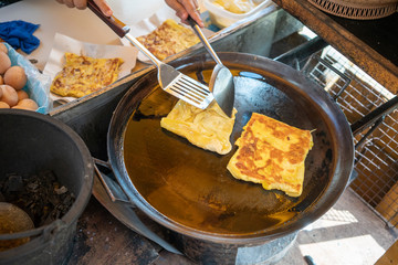 Hand cooking egg roti over hot pan with palm oil in style.