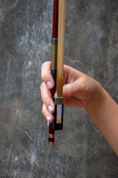 A hand holding a Violin Bow. The close up photo of Violinist holding a violin instrument with the other hand.