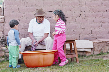 Elderly native american man washing clothes in the countryside while his two grandchildren observe him.