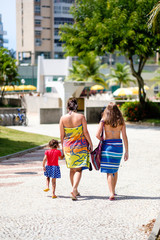 Fototapeta na wymiar two women and todler walking towards pool in bathing suits and towels during summer