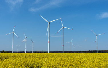 Wind power plants in a field of blooming oilseed rape seen in rural Germany
