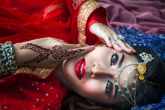 Beautiful face female with make up in Indian dress laying on floor covered with Indian cloth and smiling