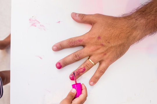 Little girl painting fathers nails pink, missing the nails and painting the fingers