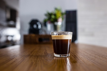 cup of fresh espresso coffee on wooden kitchen counter with interesting perspective, with cup in focus and blurred background