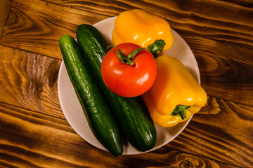 Ceramic plate with cucumbers, tomatoes and sweet pepper on wooden table. Top view