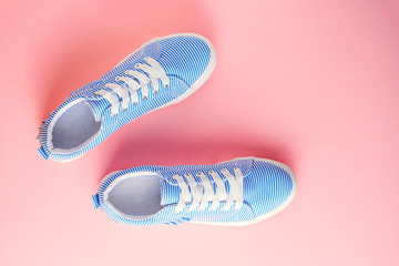 Blue striped female sneakers on pastel pink background. Flat lay, top view