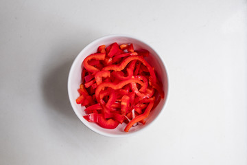 top view of sliced red bell pepper in white bowl on white counter top