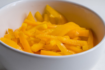diagonal close up top view of sliced yellow bell pepper in white bowl on white counter top