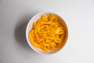 top view of sliced yellow bell pepper in white bowl on white counter top