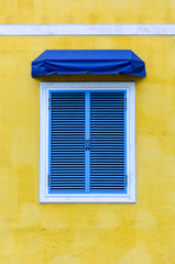 closed traditional blue greek window with white frame and blue fabric awning on yellow cement background, copy space