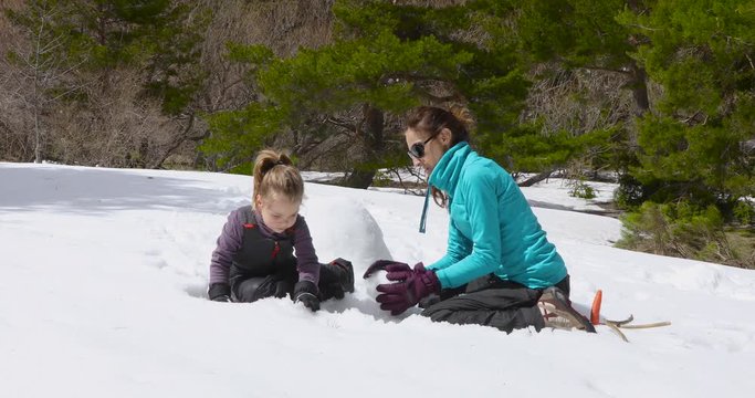 Woman mother and four years old blonde child, sitting on snow, playing making a sculpture together as teamwork in winter nature. 4k video. 

