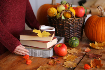 Autumn reading. stack of books, tea mug in a tray, a basket with apples and pumpkins, autumn leaves on a wooden table. Autumn season.