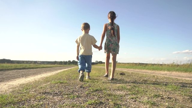 A small boy and girl holding hands are walking along the road