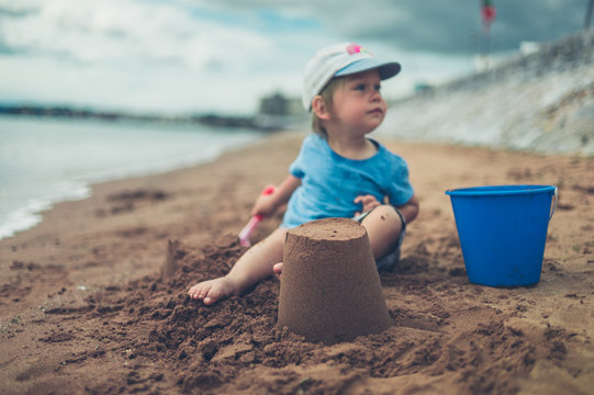Little toddler sitting on beach with sand castle