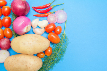organic fresh colorful vegetables with potatoes, tomatoes,coriander,chilli, onion. Minimalism on blue background.Copy space for your text.