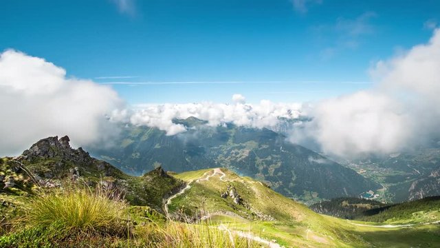 TIME LAPSE of bright green grassy hills and clouds underneath the snow covered mountains near Auron, France.