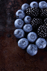 Blueberries and blackberries on a dark background, fresh berries for a vegan, fruits on a rusty background, assorted berry breakfast, copy space