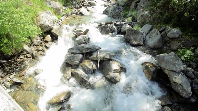 SLOW MOTION Watching a waterfall flow with blue skies and clouds in the mountains near Auron, France.