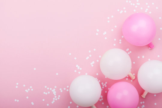 Pastel pink table with balloons and confetti for birthday from above. Flat lay composition.