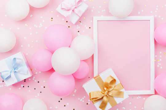 Birthday mockup with frame, gift box, pastel balloons and confetti on pink table top view. Flat lay composition.