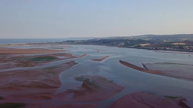Flying over the beach of Lympstone while panning from right to left to show the beautiful environment and multiple towns in the area. Aerial view of the sand and water formation.