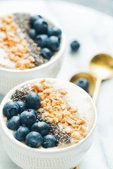 Smoothie bowls with fresh ripe blueberry, nuts, chia, banana and soya milk over white marble. The concept of healthy eating and vegetarian food.