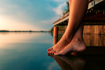 Woman legs as she sitting on wooden dock by the lake. - Powered by Adobe