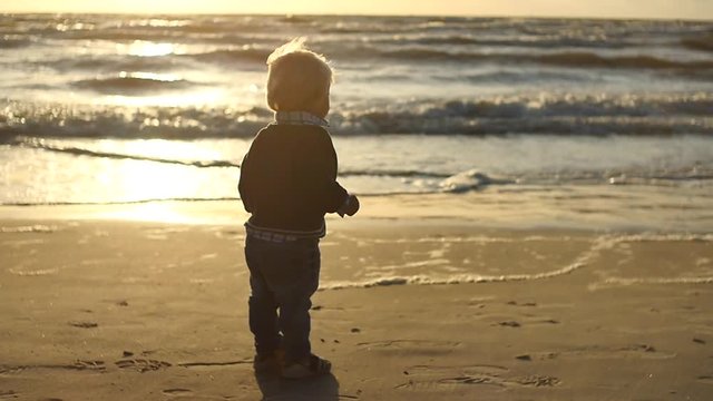 cute 1.5 years old baby standing near waving sea coast - filmed against sun