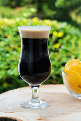 A glass of cold dark beer on wooden table in the garden