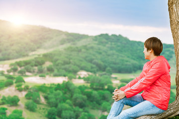 A woman sitting under a tree looking over the mountain