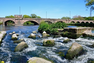 View across boulders and the weir towards the Trent Bridge road bridge A511 over the River Trent, Burton upon Trent, UK.