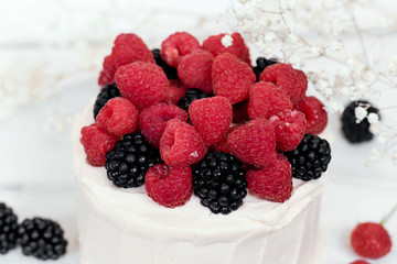 Cake with raspberries and blackberries on white wooden background.