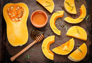 Sliced raw organic butternut squash on a baking pan with honey and rosemary