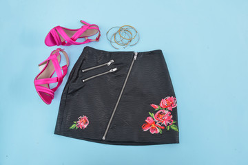 Close up embroidered, flowers black leather skirt  with pink shoes on blue background