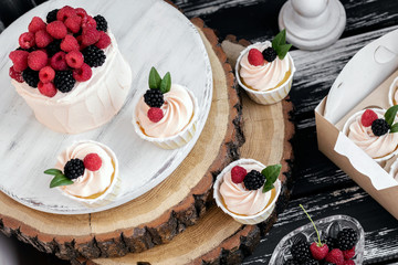 Cake and muffins with raspberries and blackberries on wooden background.