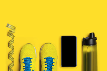 Flat lay shot of Sport equipment. Sneakers, water, earphones and phone on yellow background. Focus is only on the sneakers
