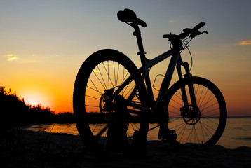 Fototapeta na wymiar Silhouette of bicycle on the beach against colorful sunset in the sea, gold sky background. Reflection of sun in water. Outdoors.