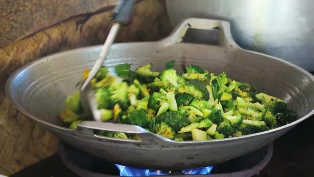 Broccoli being stirred in a steel wok, over an open flame.