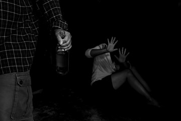 Fototapeta na wymiar Woman victim of domestic violence and abuse. Woman scared of a man holding alcohol bottle.