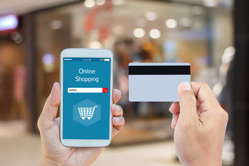 Hand holding smart phone with online shopping on screen and credit card over blurred in shopping mall background for mobile banking payment online concept