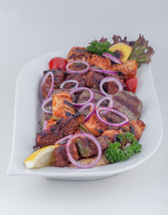 Traditional Arabic mixed grill platter with grilled meat skewers, steak served with cherry tomato,  onion, broccoli and lemon in a white plate on white background
