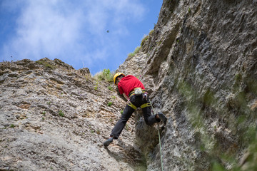 Obraz premium Photo from back of climbing young sports guy in yellow helmet on rock at summer day